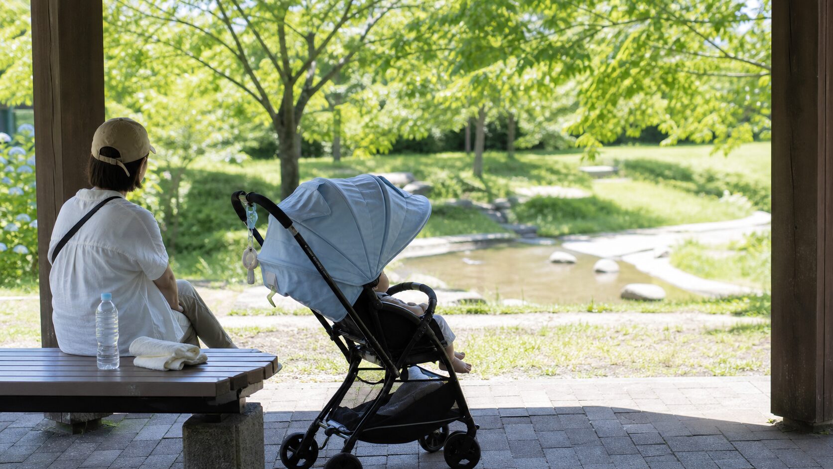 夏の公園の日陰でベビーカーと親子が短く休憩するイメージ