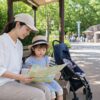 夏の動物園か遊園地で子ども連れの家族が日陰で休憩しながら外出計画を立てるイメージ