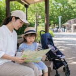 夏の動物園か遊園地で子ども連れの家族が日陰で休憩しながら外出計画を立てるイメージ
