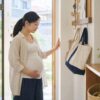 夏の朝に保育園バッグとメモを確認しながら玄関で休み方を整える妊婦のイメージ