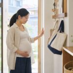 夏の朝に保育園バッグとメモを確認しながら玄関で休み方を整える妊婦のイメージ
