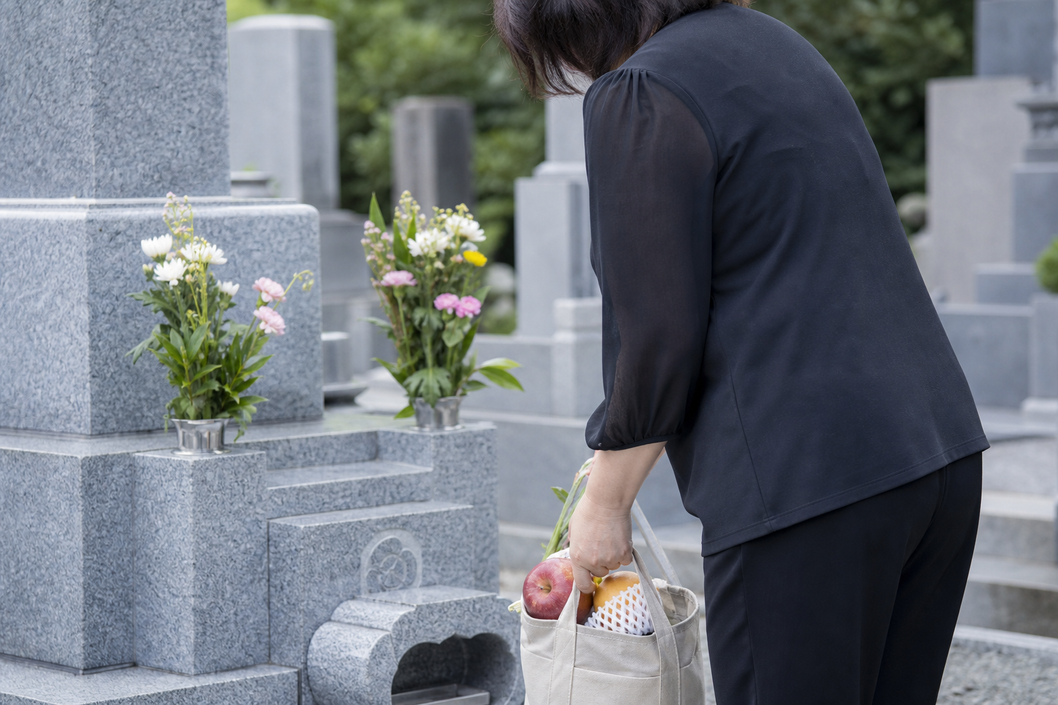 墓前で参拝後にお供え物を持ち帰る準備をする後ろ姿の落ち着いたイメージ