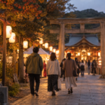 秋祭りの提灯が並ぶ夕方の境内へ歩く人々の後ろ姿