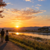 秋分の頃の夕日を川辺で眺める二人の後ろ姿