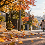 秋の住宅街で落ち葉が風に舞いコート姿の人が歩く様子