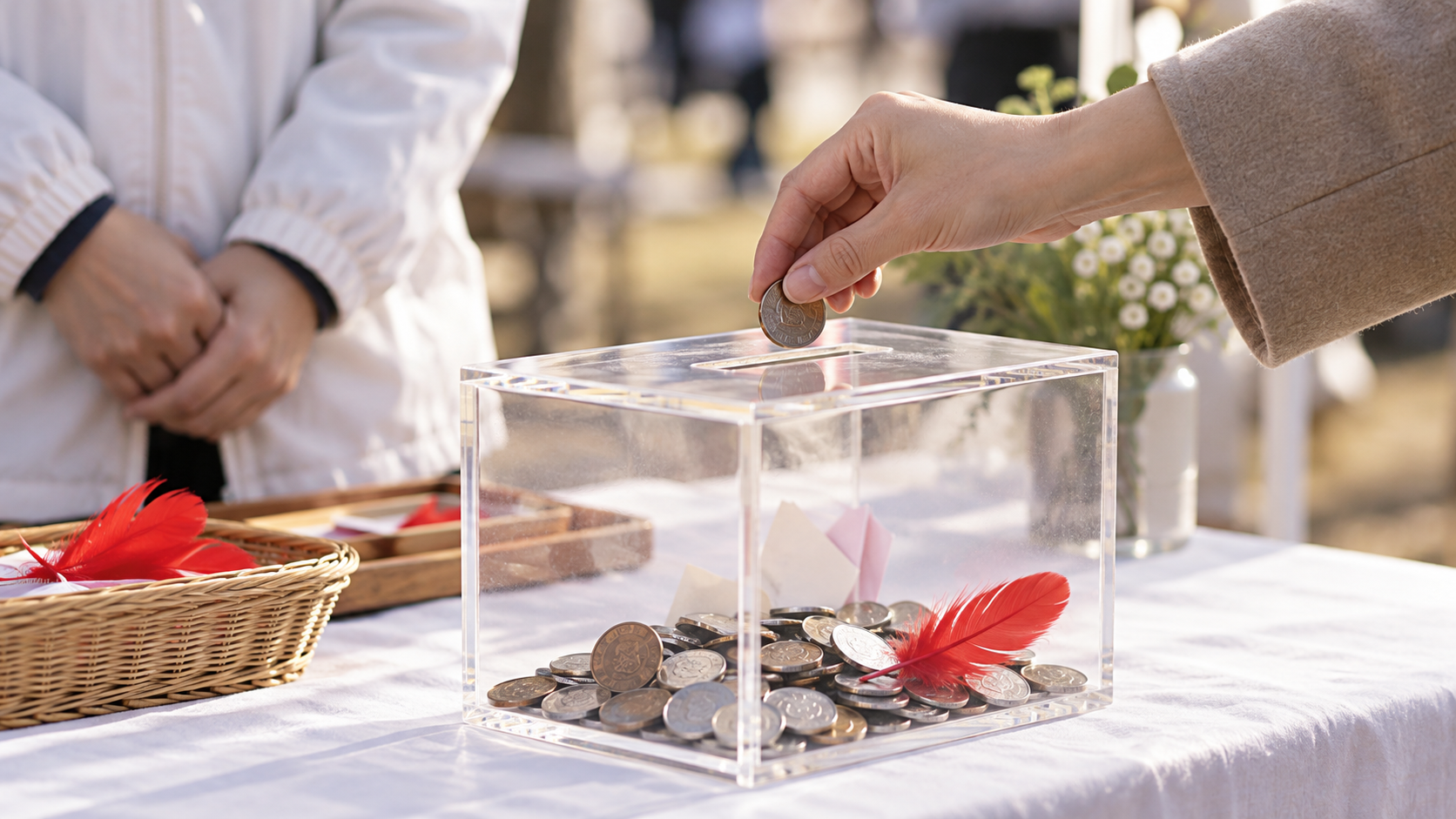 透明な募金箱に硬貨を入れる手元と赤い羽根